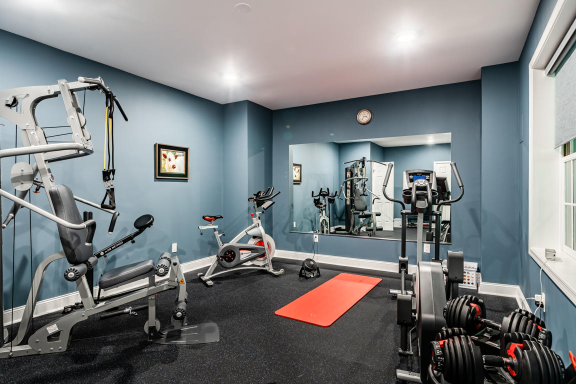 Carriage Path home gym — rubber flooring, large wall mirror, cable machine, recessed lighting