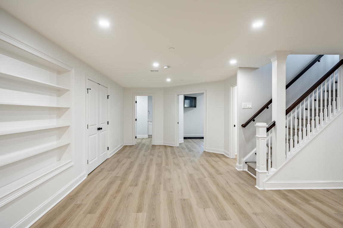 Open finished basement at Plymouth Road with LVP flooring, custom built-in shelving, white trim, and open staircase