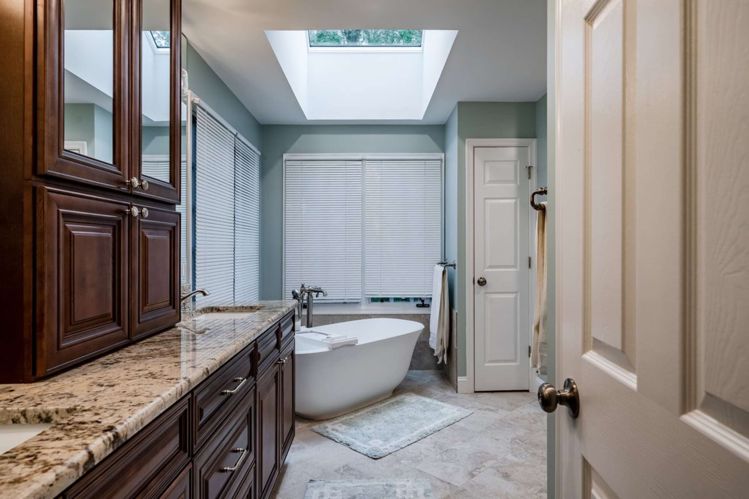 Chadds Ford full bathroom with freestanding soaking tub, skylight, dark wood vanity, and granite countertops