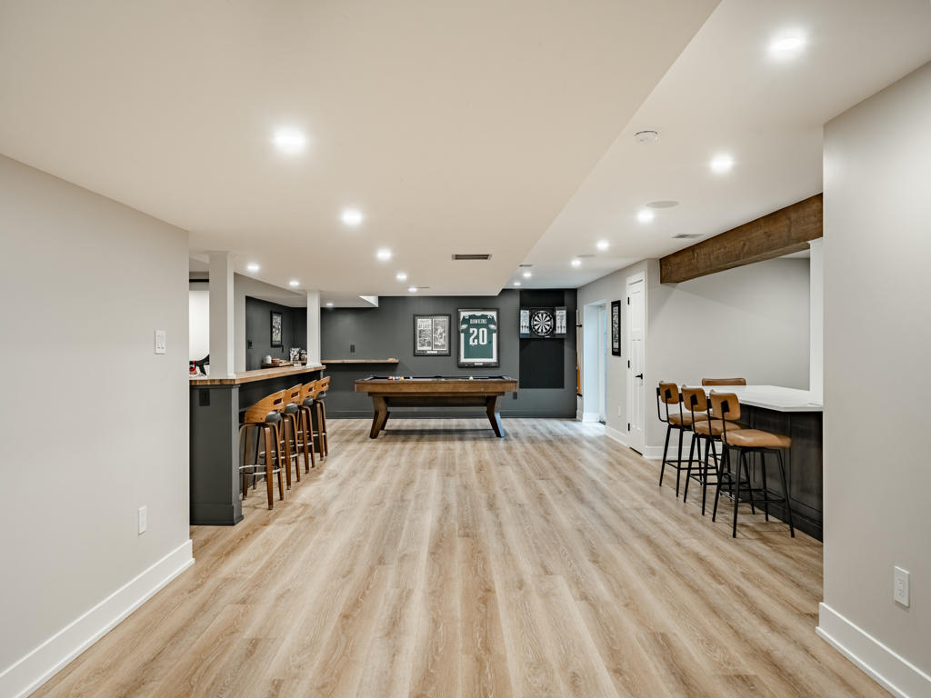 Wide angle view of finished Chester Springs basement remodel showing pool table game room, dual bar areas, and charcoal accent wall with Eagles memorabilia