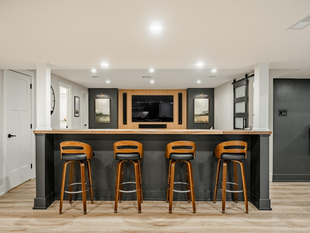 Swivel bar counter with custom black walnut butcher block top and mid-century swivel bar stools facing the basement home theater media wall