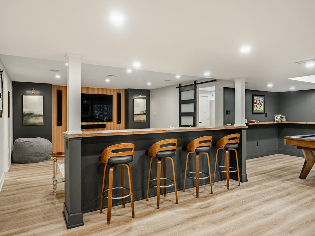 Basement entertainment area showing swivel bar counter with butcher block top, slatted TV accent wall, and pool table in background