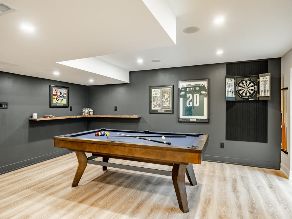 Basement game room with pool table, dark charcoal accent wall, framed Eagles jersey, dart board cabinet, and floating wood corner ledge