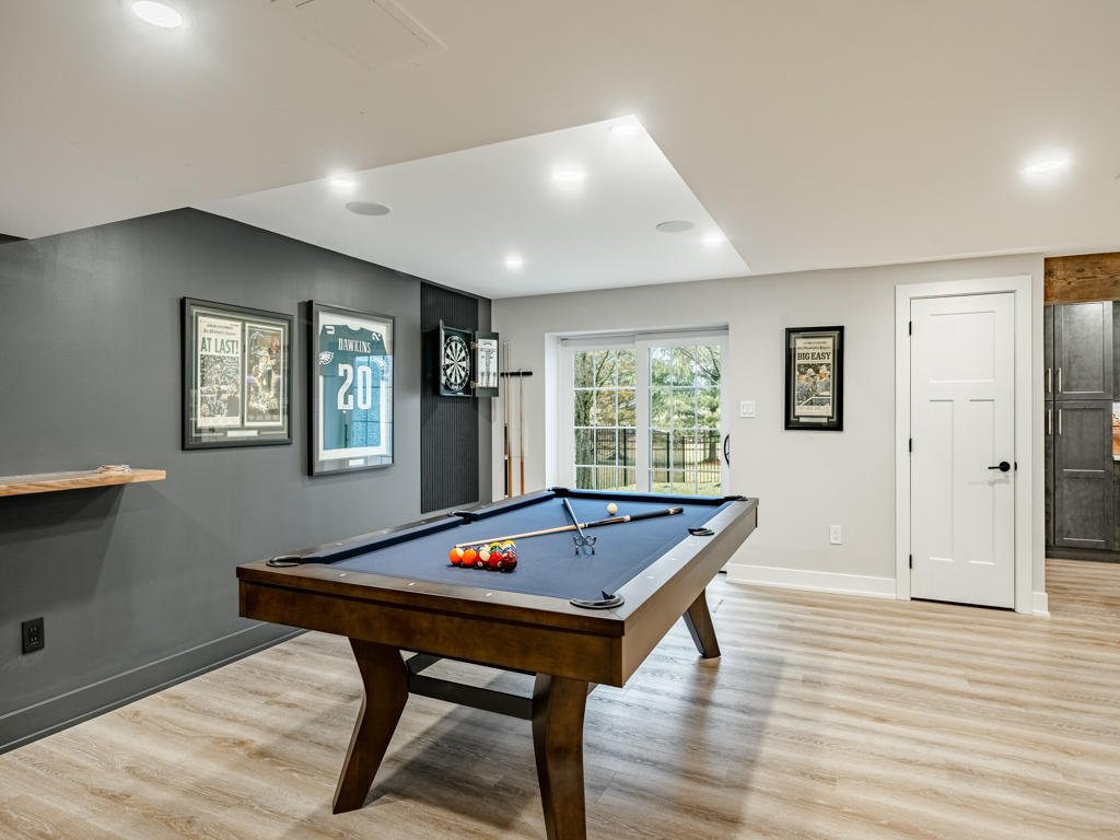 Pool table game room with charcoal accent wall, framed Eagles memorabilia, dart board, and walk-out basement egress window