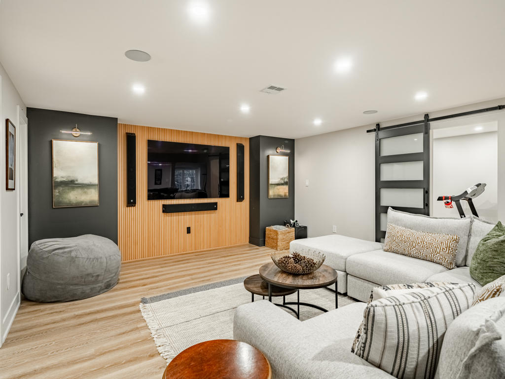 Lounge seating area with slatted wood TV wall, black frosted-glass barn door, and gray sectional sofa in Chester Springs finished basement