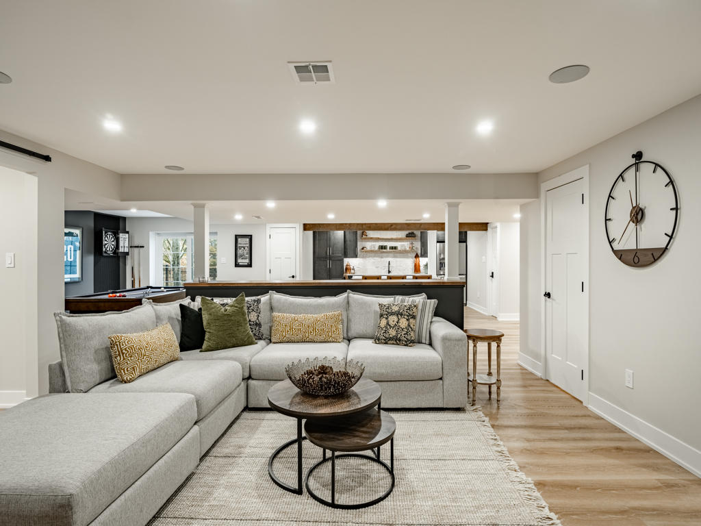 Basement lounge and entertainment zone from seating area showing full open layout with TV wall, game room, and wet bar beyond