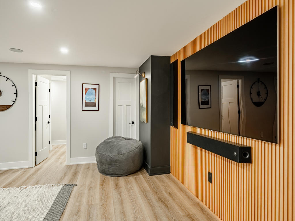 Close-up of slatted natural wood TV accent wall with flush-mounted large-format television and soundbar in basement home theater zone