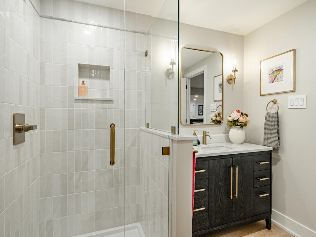 Frameless glass walk-in shower with vertical white glazed tile, brass hardware, and built-in shower niche in Chester Springs basement bathroom