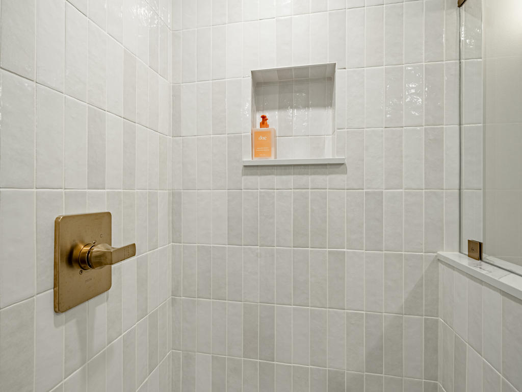 Shower interior detail showing vertical white tile walls, brushed brass thermostatic valve, and recessed niche in Chester Springs basement bathroom