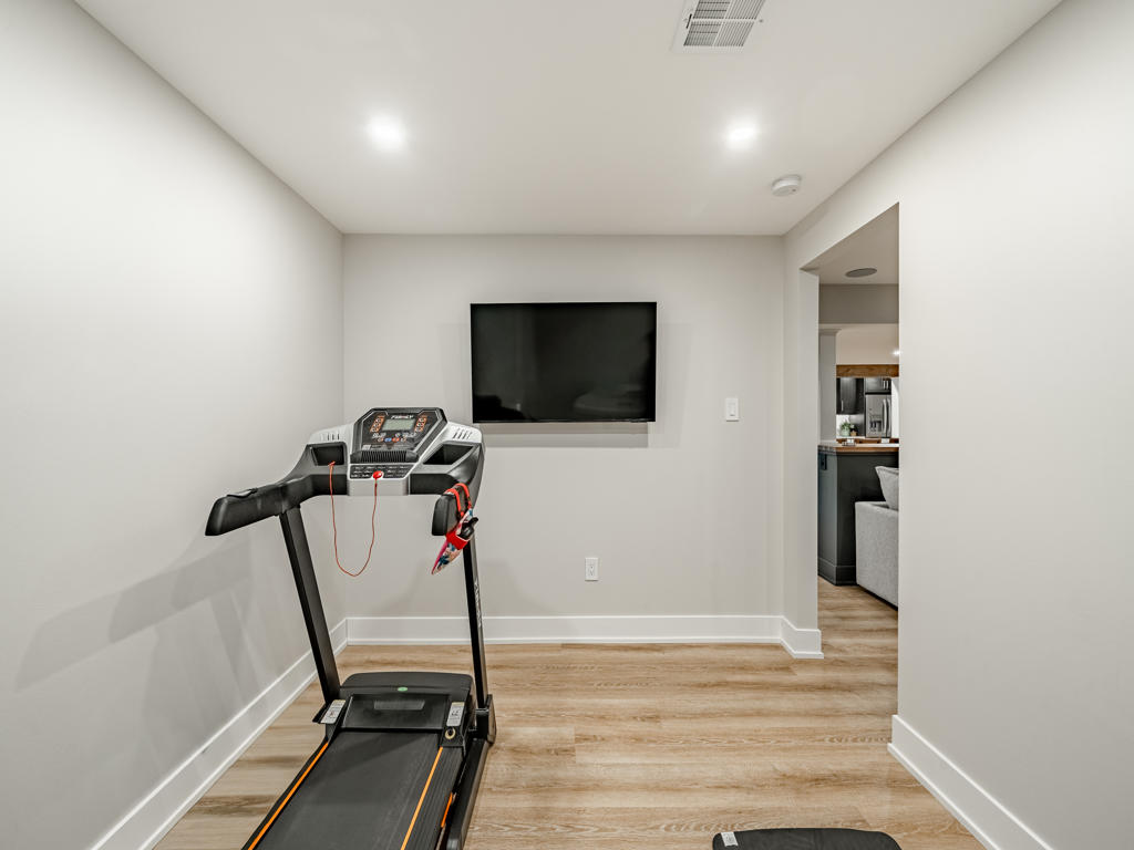 Basement fitness room with treadmill and wall-mounted TV, open to main living area through arched doorway