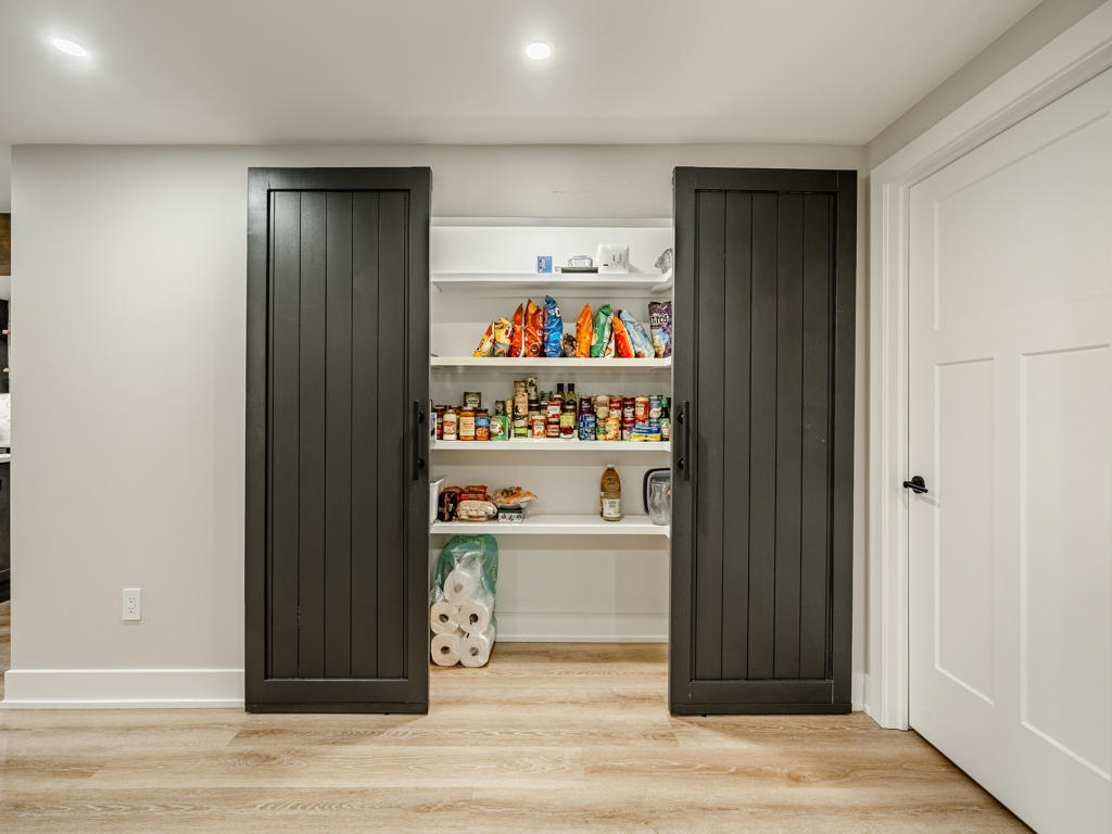 Custom concealed basement pantry with dark shiplap double doors open revealing deep white built-in shelving and abundant storage