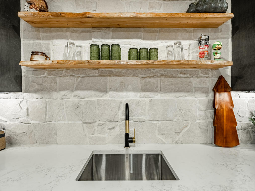 Undermount stainless sink with matte black and brass pull-down faucet set against natural ledger stone backsplash and white quartz countertop