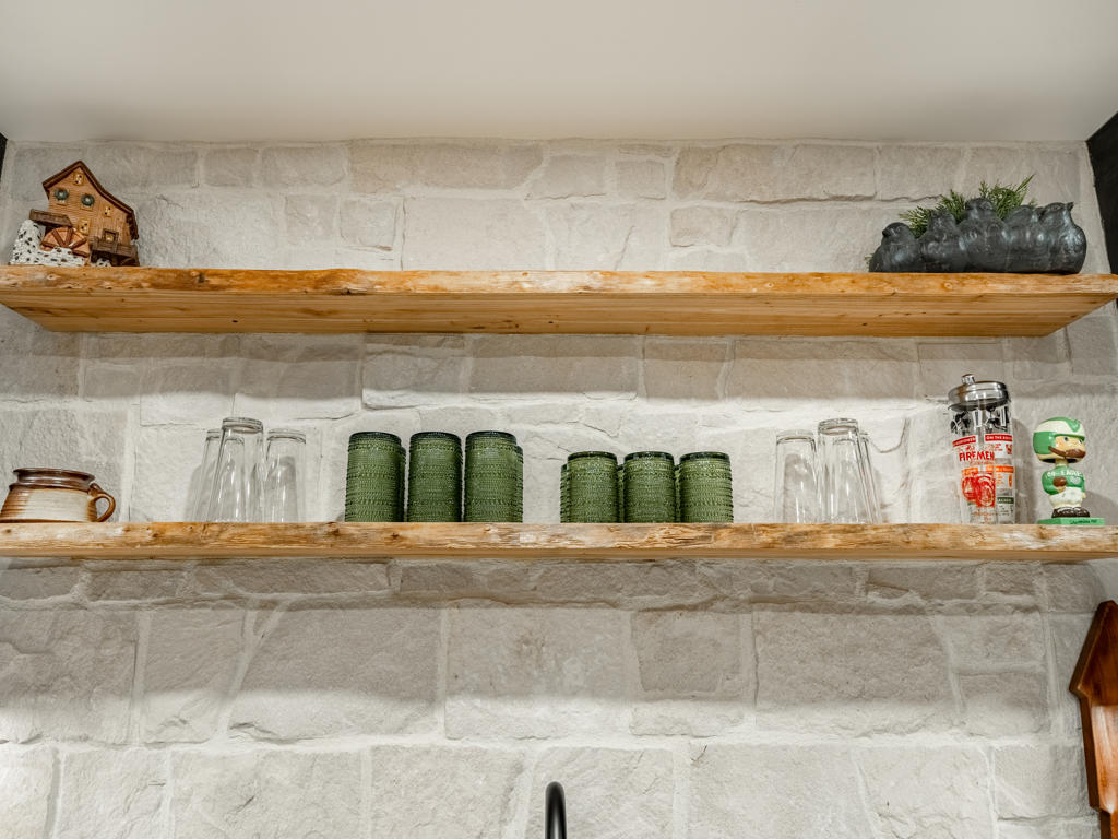 Floating live-edge wood shelves in front of natural ledger stone backsplash in Chester Springs basement wet bar