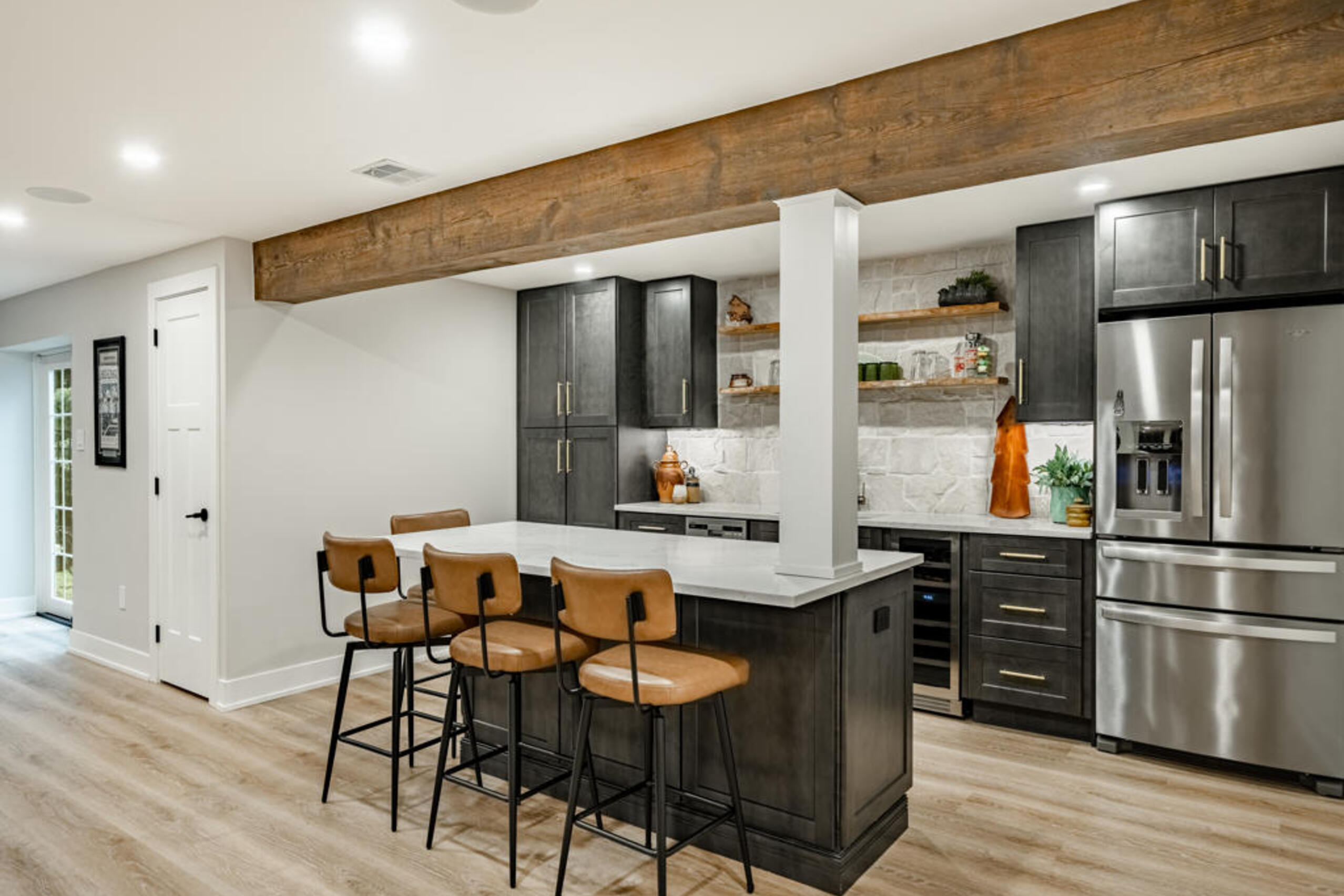 Custom wet bar with charcoal shaker cabinets, natural stone backsplash, and floating live-edge shelves in Chester Springs basement