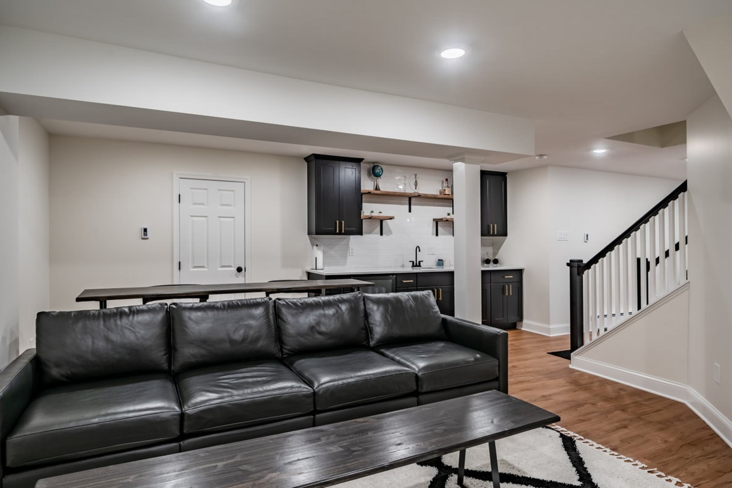 Chester Springs basement remodel with black cabinets, leather sofa, wet bar, and hardwood floors