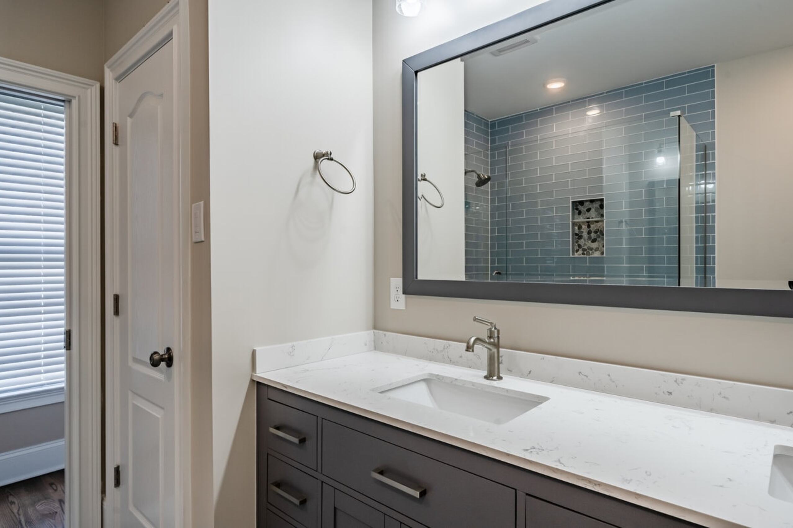 Downingtown master bathroom vanity with dark shaker cabinets, quartz countertop, and blue subway tile shower reflected in mirror