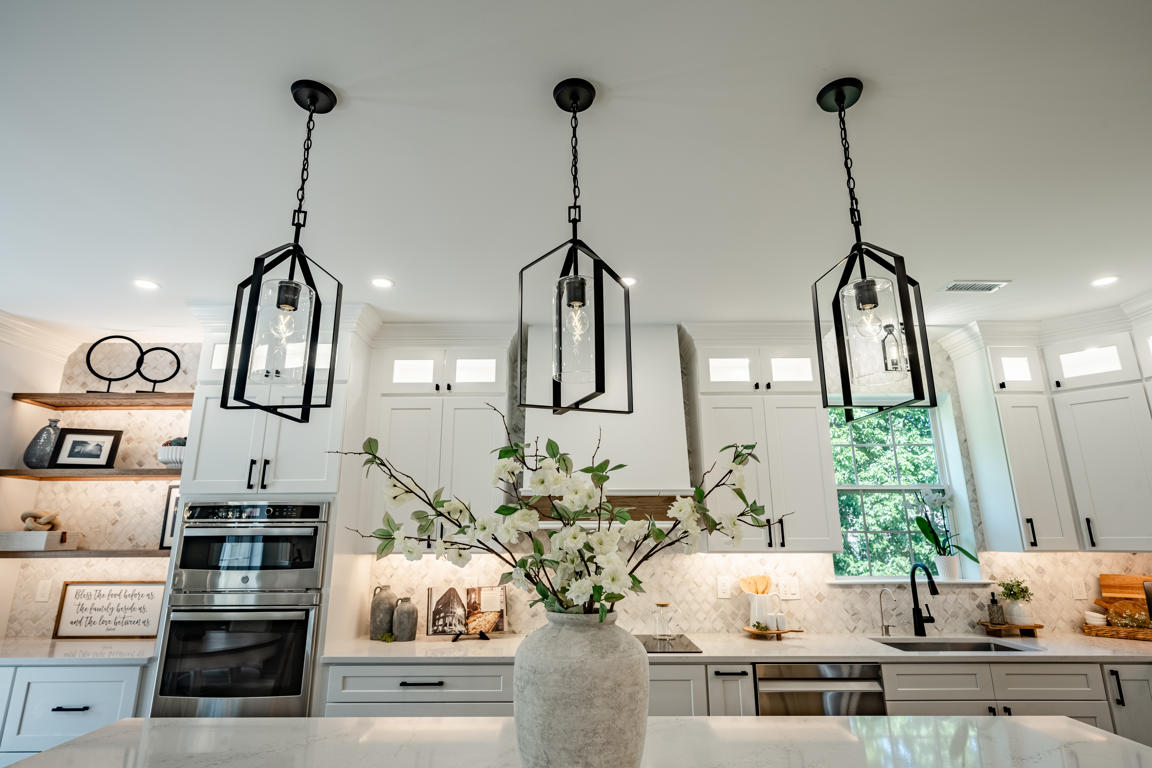 Upper cabinet detail with white shaker doors, matte black pulls, illuminated transom windows above, and arabesque marble backsplash below