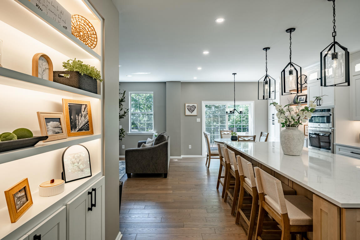 Stacked wall oven tower in white shaker cabinetry with dining area visible beyond, hardwood floors running throughout open floor plan