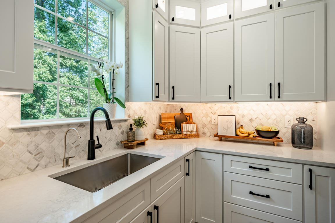 Corner sink close-up with undermount stainless steel basin, matte black faucet, arabesque marble backsplash, and window with garden view