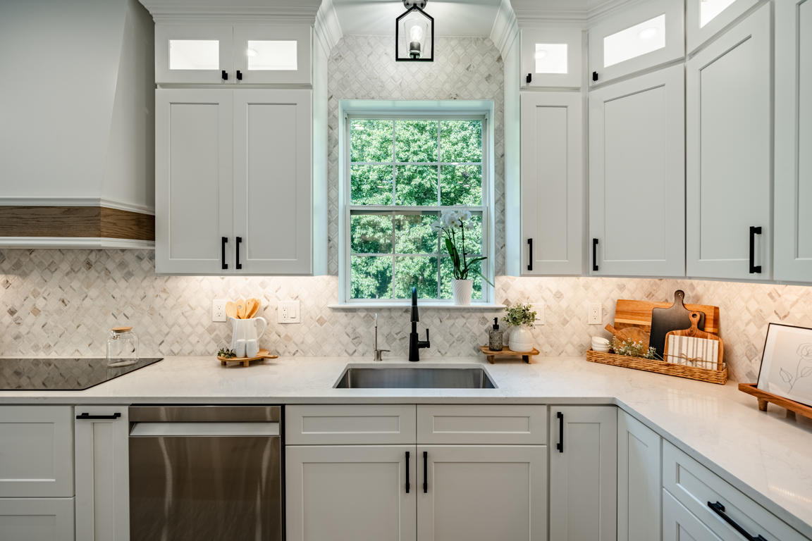 Kitchen sink wall symmetrical view with centered window, arched backsplash detail above window, arabesque marble mosaic, and matte black pendant light
