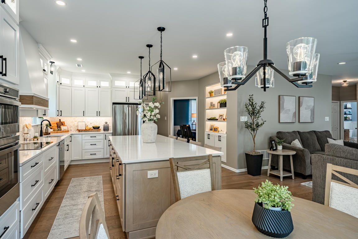 Downingtown Montana Drive kitchen and living room remodel by Craftsworth Construction - wide view of two-tone kitchen with natural wood island, white perimeter cabinets, lantern pendants, arabesque marble backsplash, built-in living room shelving with accent lighting, and open concept layout