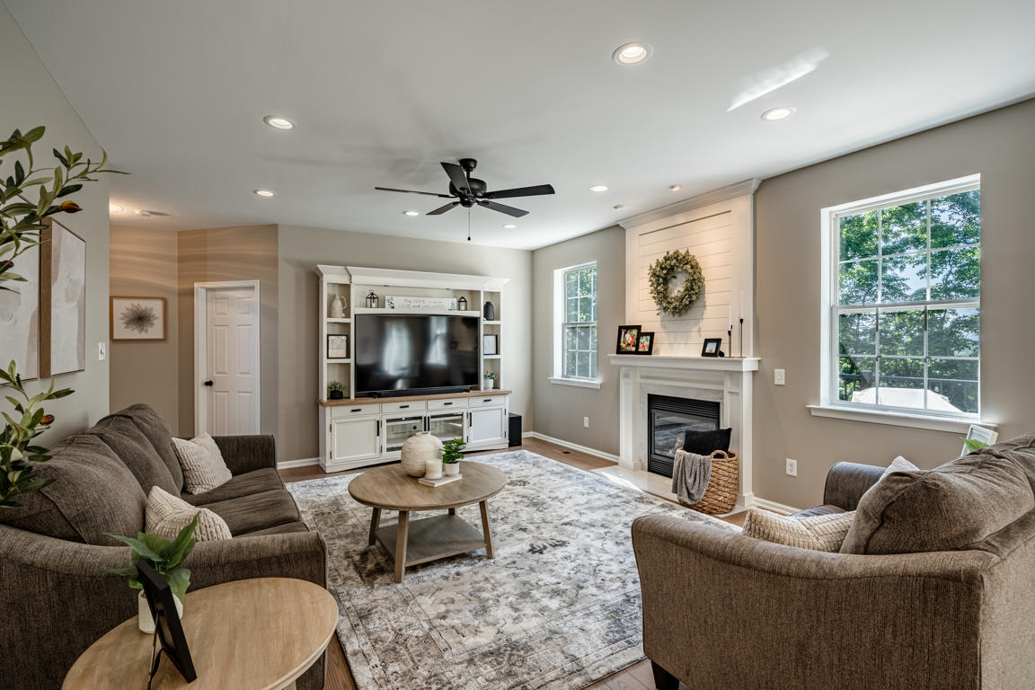 Living room with shiplap fireplace surround, preserved eucalyptus wreath on white mantel, built-in media center, ceiling fan, and plush seating