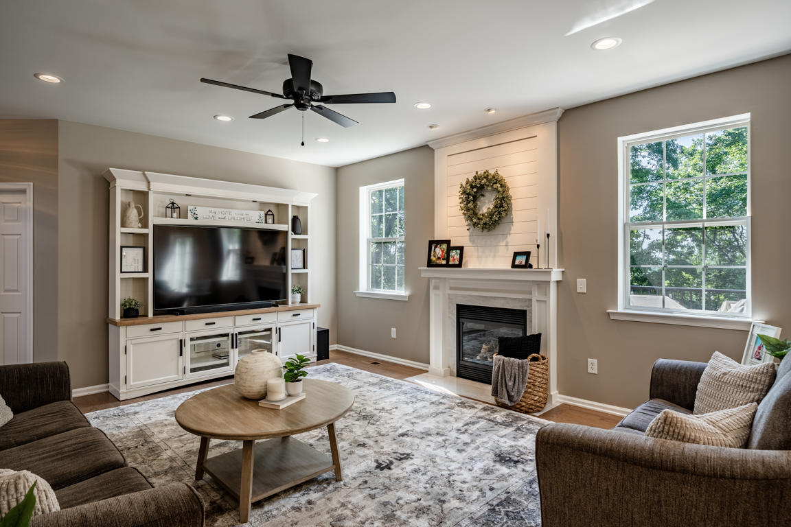 Living room alternate angle showing shiplap fireplace, flanking windows with natural light, entertainment center with oak-topped cabinet, and area rug