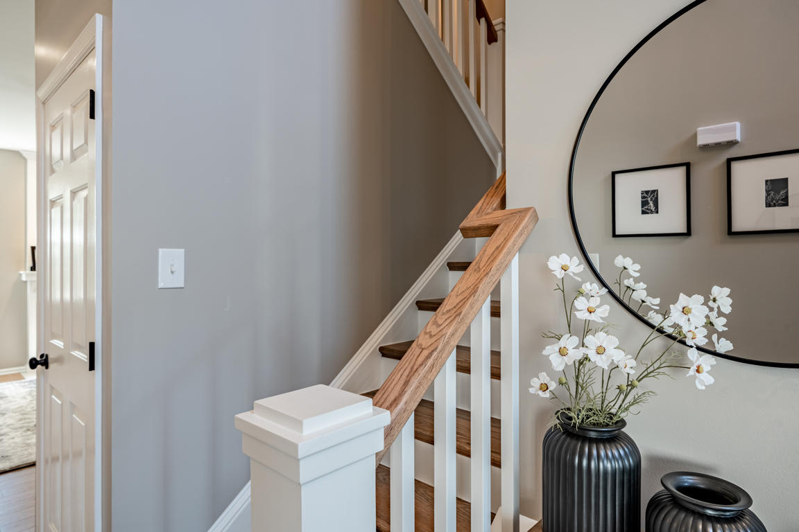 Staircase detail showing white painted balusters, stained oak handrail, round black mirror, and black-framed art gallery on adjacent wall