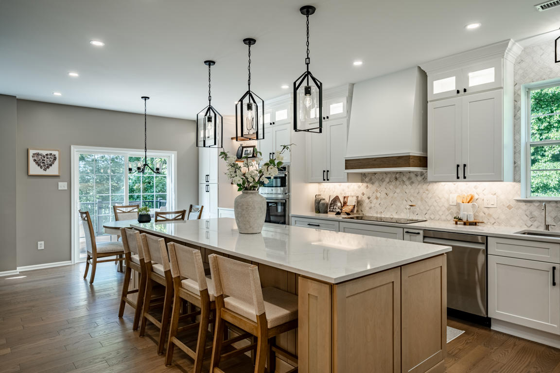 Two-tone kitchen galley view between natural wood island and white perimeter cabinets with arabesque marble backsplash and under-cabinet lighting