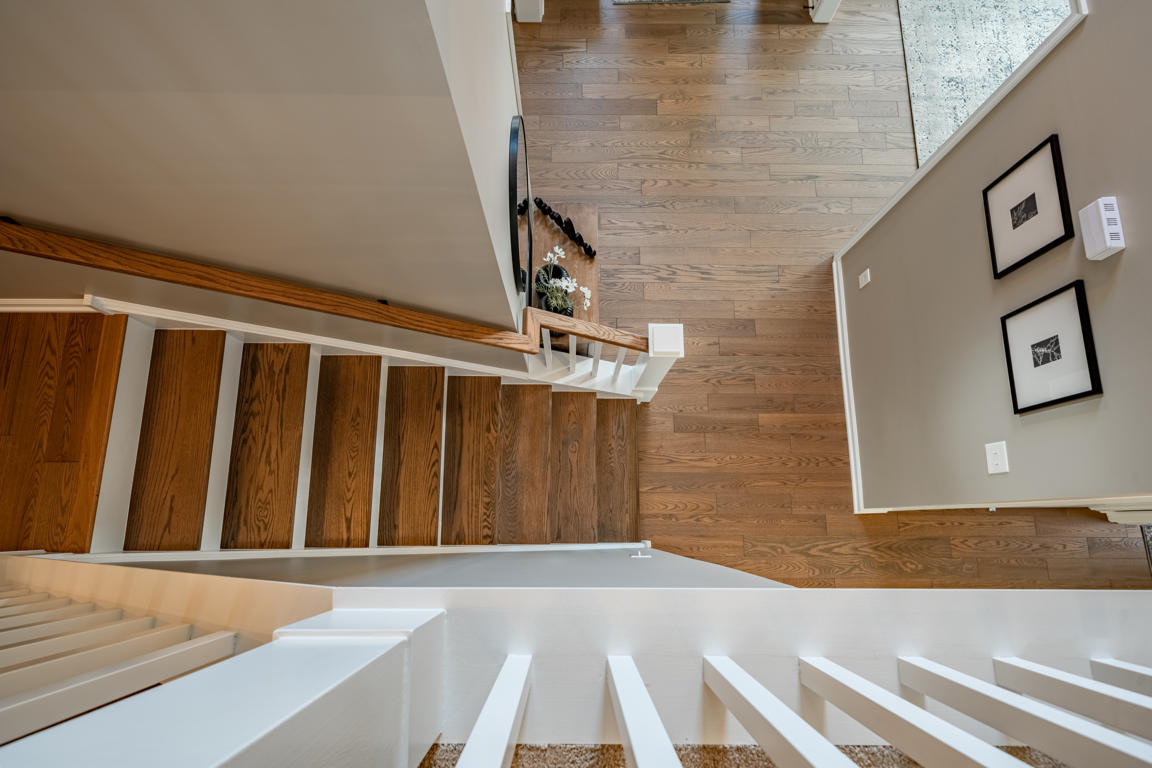 Second floor overlook down through two-story stairwell showing refinished hardwood floors, white balusters, stained oak treads, and entry below