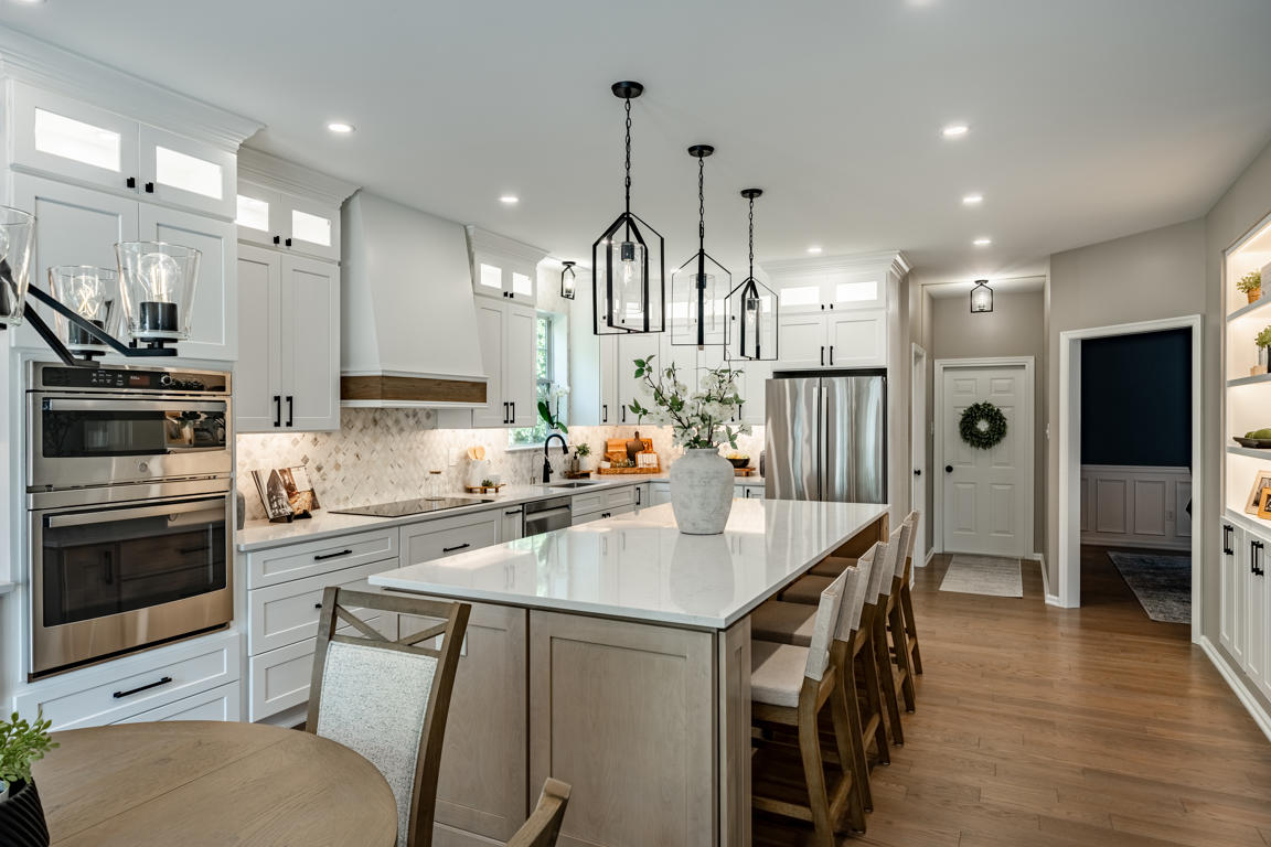 Black iron lantern pendant lights in geometric cage design hanging above natural oak kitchen island with clear glass panels