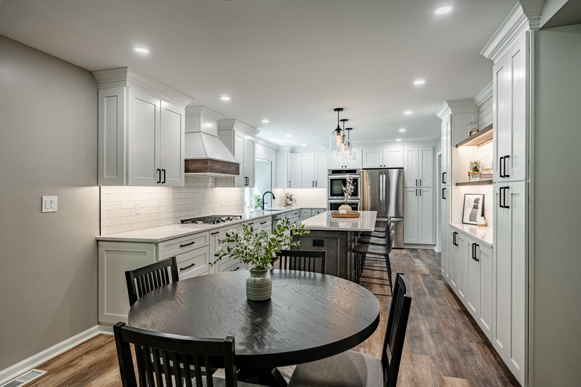 Wide angle of complete Exton PA kitchen remodel showing white cabinetry, dark island, subway tile, pendant lights, and rustic wood-look LVP flooring