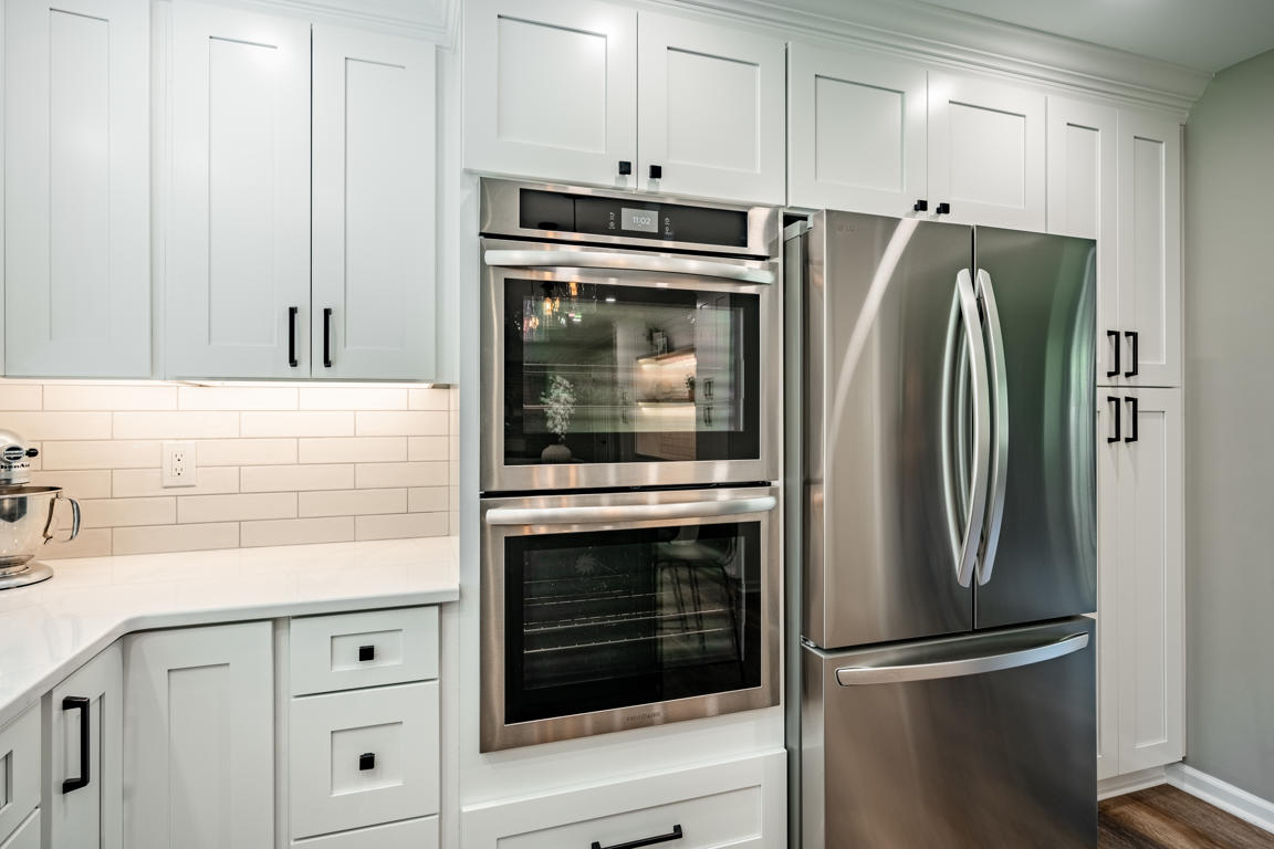 Stainless steel double wall ovens and French door refrigerator flanked by white shaker pantry cabinets