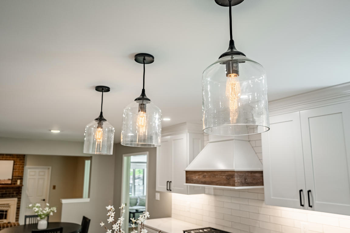 Glass bell jar pendant lights with vintage Edison filament bulbs over kitchen island and custom range hood