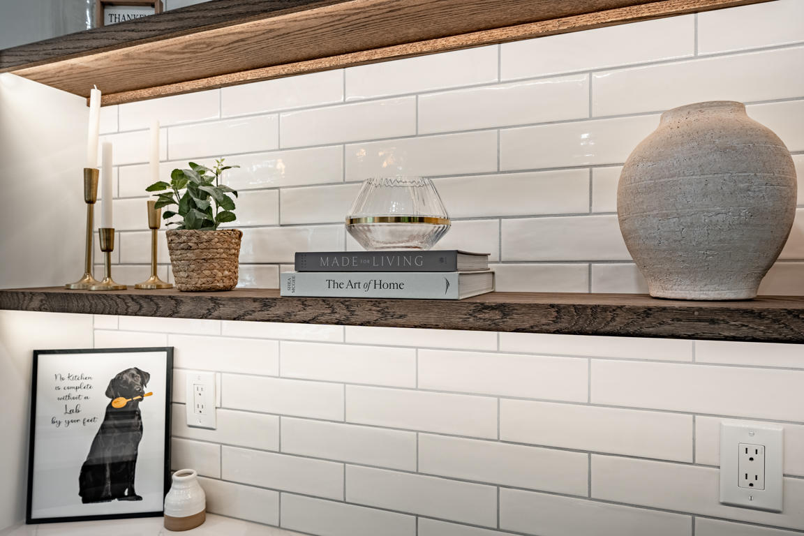 Decorative shelf styling with design books, woven basket planter, glass bowl, and ceramic vase against subway tile
