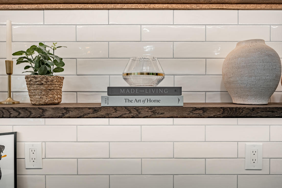 Floating rustic wood shelf detail with curated decor against white subway tile