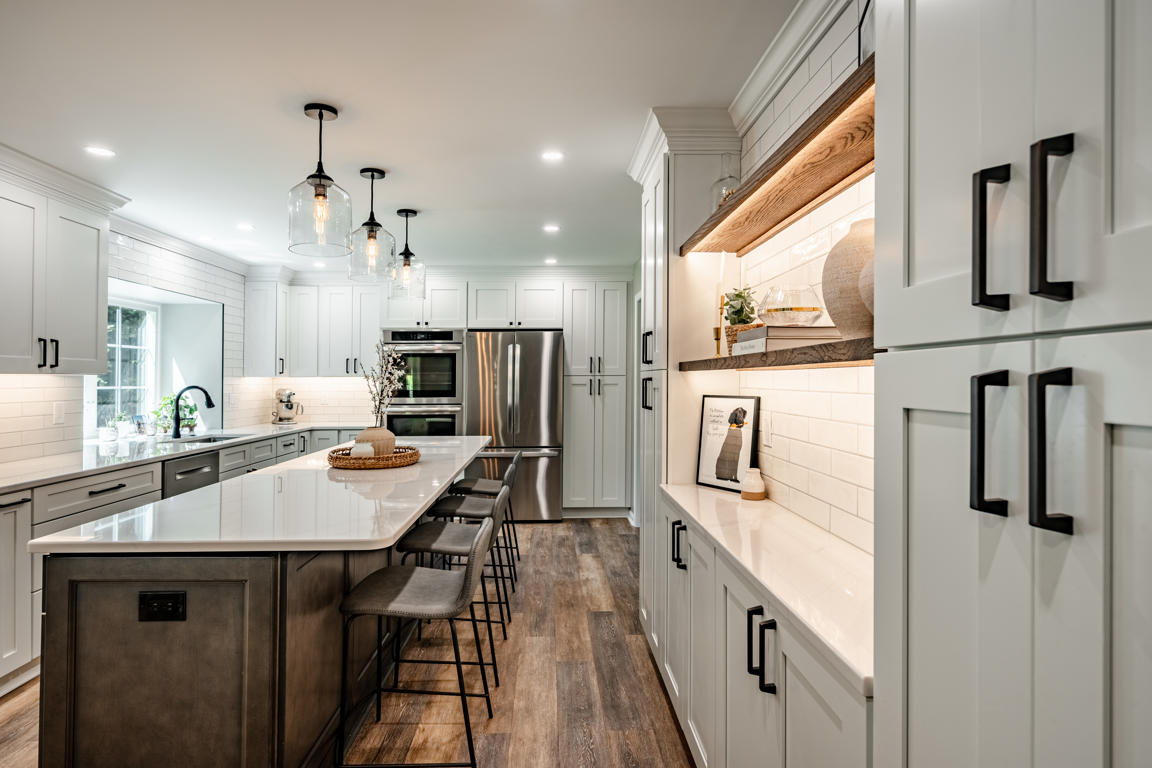 End view of kitchen island with stainless French door refrigerator, double wall ovens, and quartz countertops