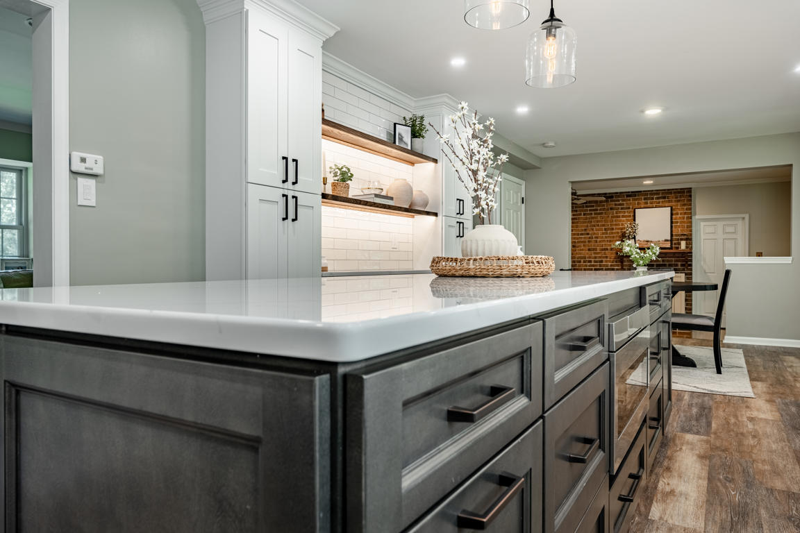 Dark stained kitchen island with quartz countertop and view toward display niche with floating shelves