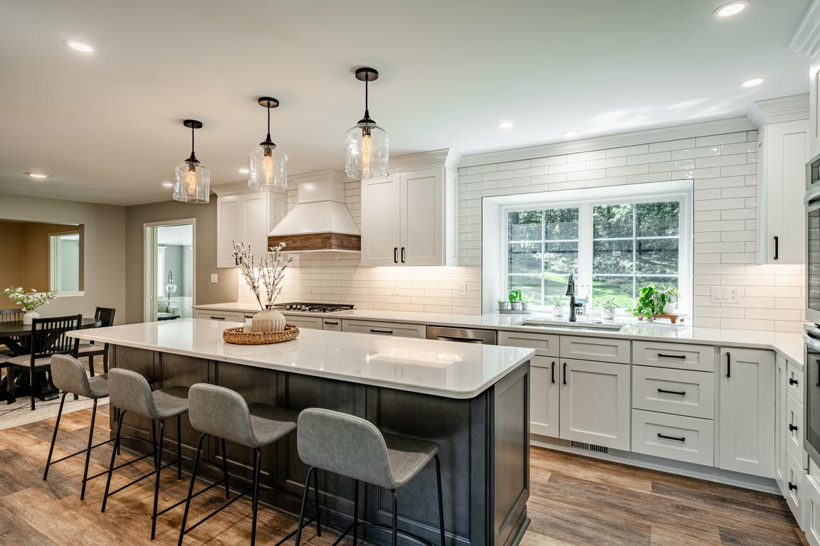 Large kitchen island with gray upholstered bar stools, white quartz countertops, and glass pendant lighting in Chester County home