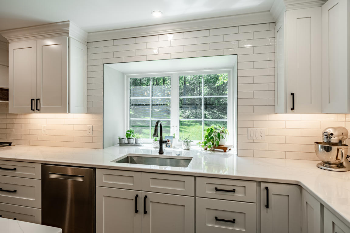 Undermount stainless steel sink with oil-rubbed bronze gooseneck faucet and large window overlooking wooded backyard