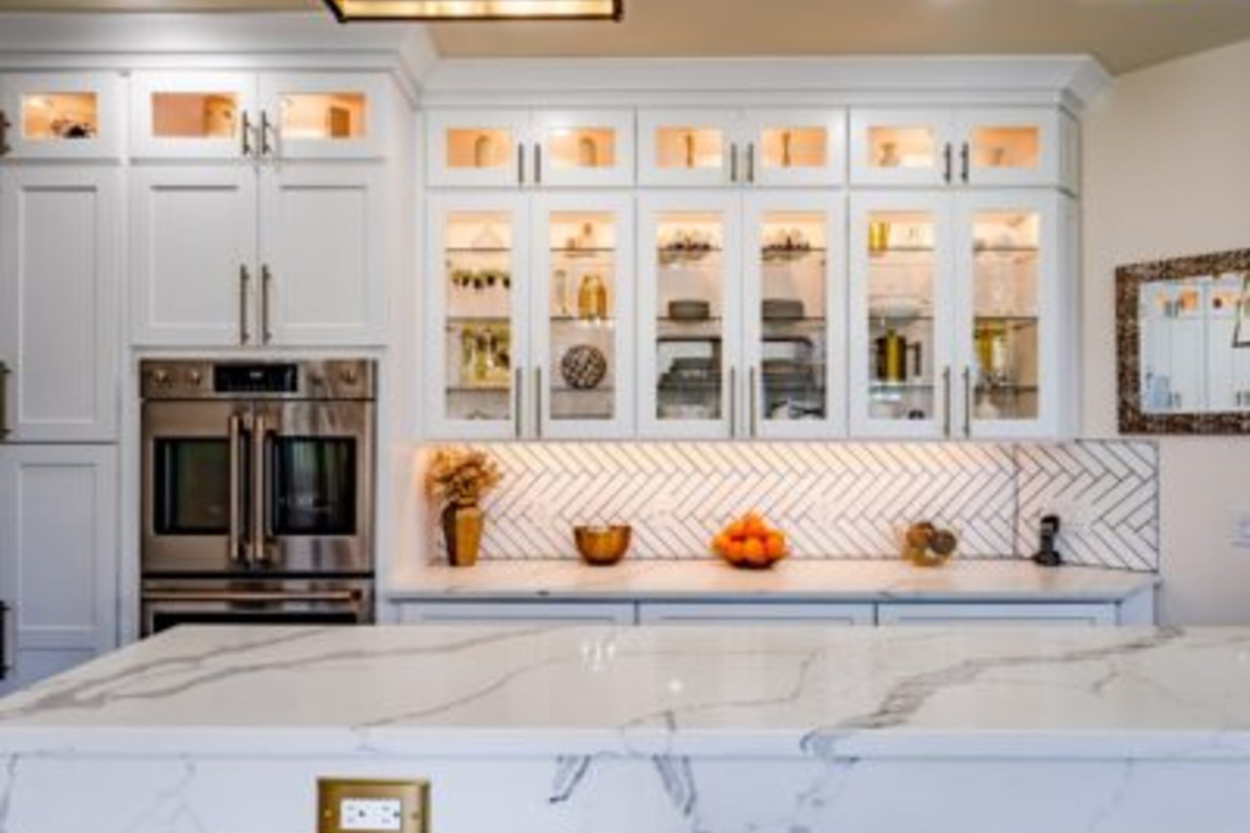 Glenmoore kitchen glass-front display cabinets with interior lighting, herringbone backsplash, and marble countertops