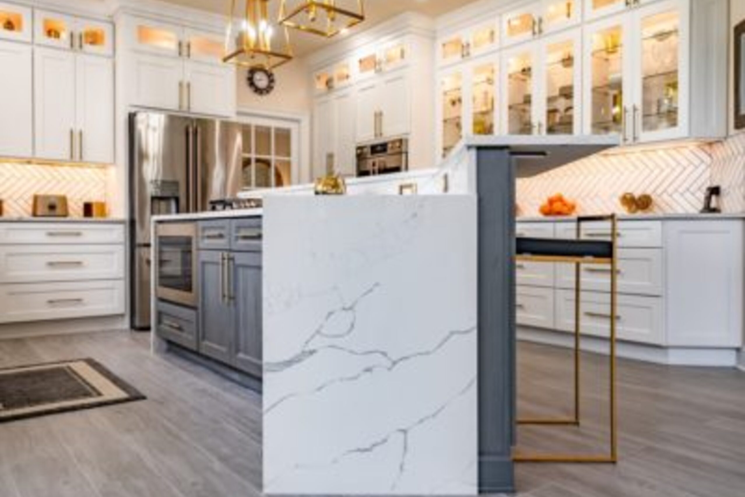 Glenmoore luxury kitchen with marble waterfall island, gray base cabinets, glass-front uppers, and gold pendants