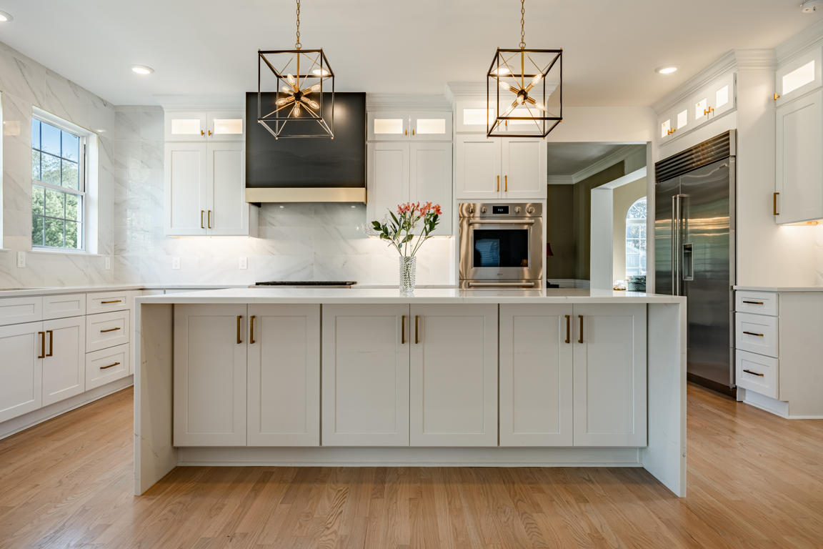 Range wall composition with matte black and gold hood, marble backsplash, and flanking white cabinets with gold hardware