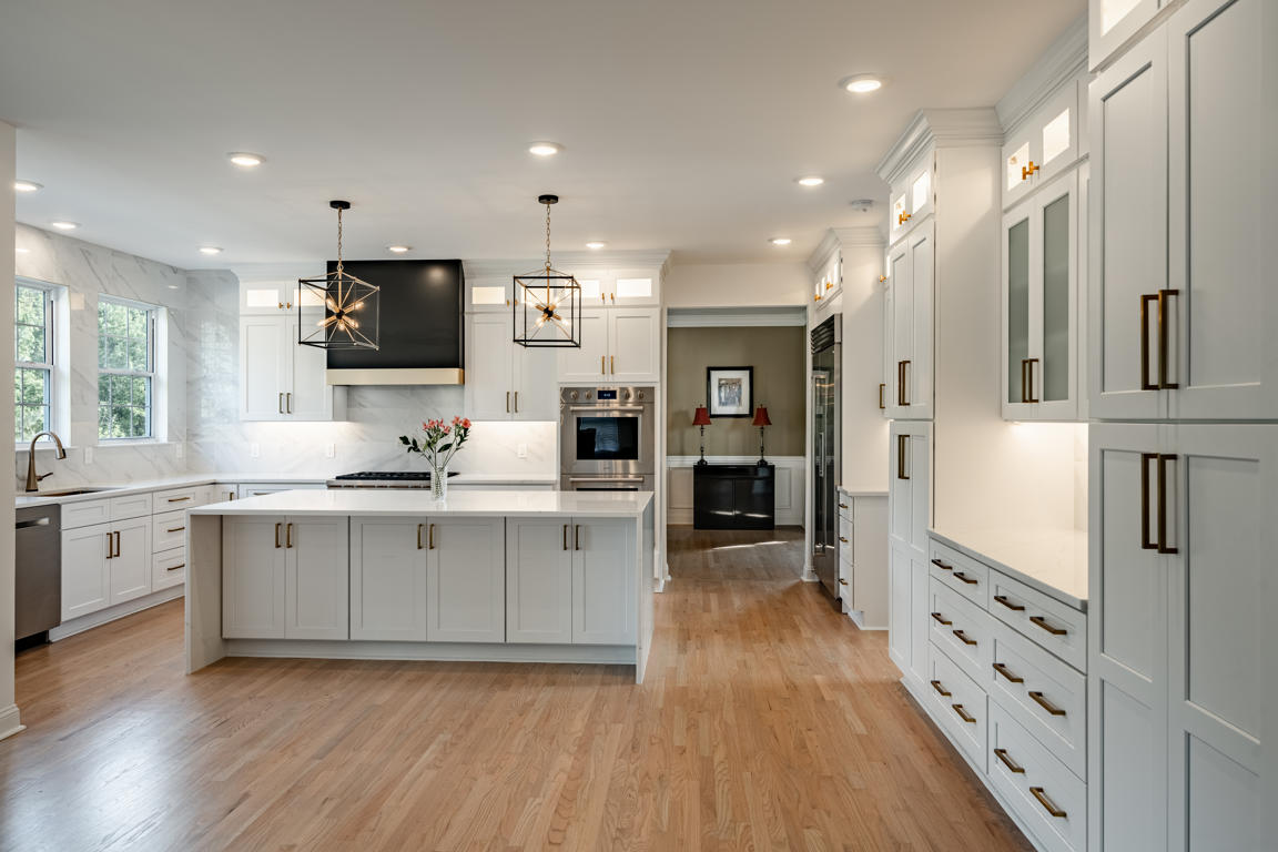 Kitchen island detail showing quartz countertop with marble veining, white shaker drawers with brushed gold bar pulls, and built-in microwave drawer