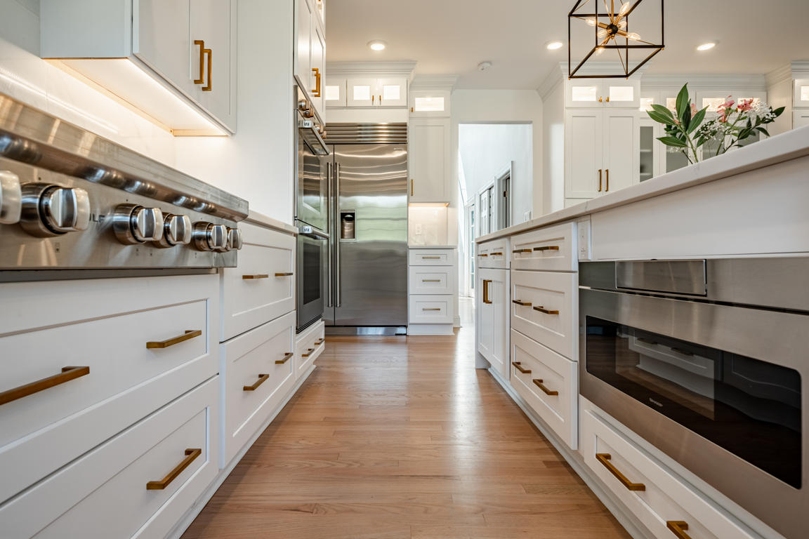 Galley view between island and perimeter cabinets showing professional range, built-in refrigerator, and hardwood floors