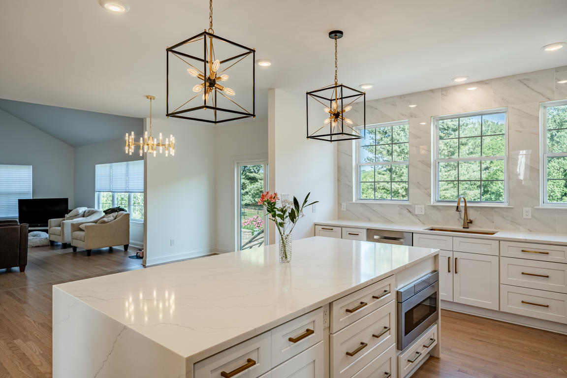 Kennett Square kitchen remodel by Craftsworth Construction - wide view of quartz waterfall island with geometric cage pendant lights, white shaker cabinets with brushed gold hardware, marble-look porcelain backsplash, and open concept layout to living area