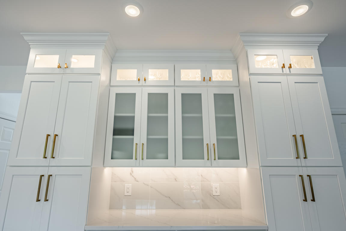 Glass-front display cabinetry with frosted glass doors, brushed gold hardware, illuminated shelves, under-cabinet lighting, and marble backsplash