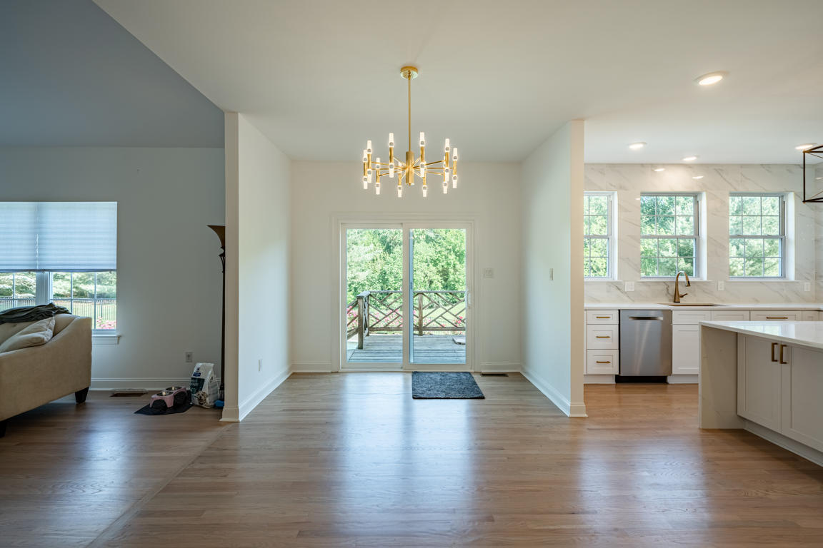 Dining area adjacent to kitchen with French doors to deck, modern brass chandelier, hardwood floors, and open floor plan