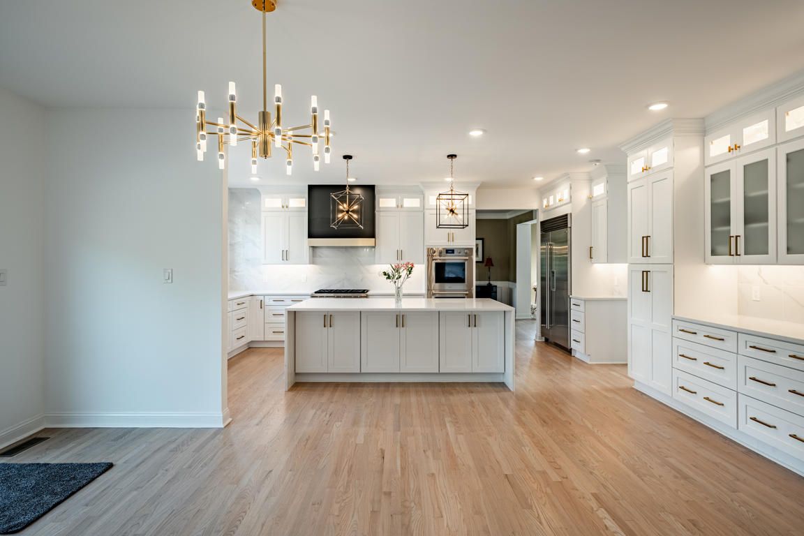 Professional-grade stainless steel range with oversized control knobs flanked by white shaker cabinets and brushed gold hardware