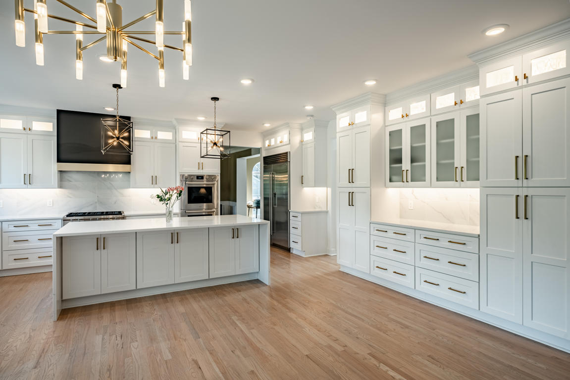 Matte black and brushed gold range hood above marble-look porcelain tile backsplash with white shaker cabinets flanking